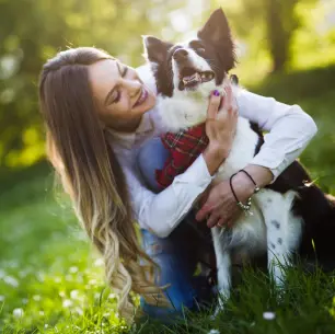 A long-haired brunette woman kneels next to her dob wearing a red bandana outside on the grass while hugging him.